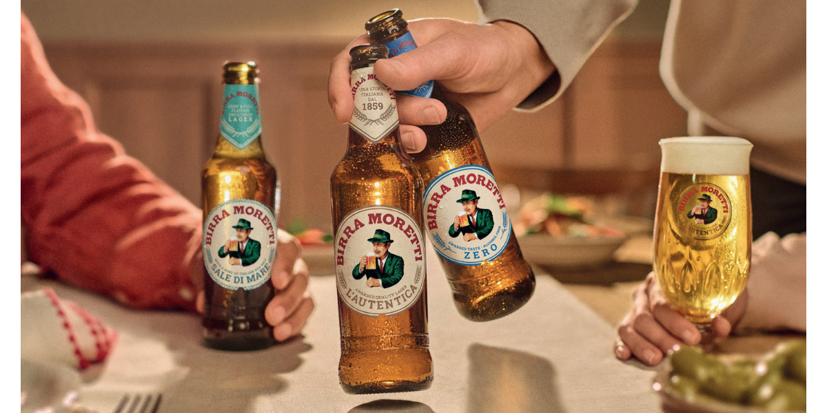 Three bottles of Birra Moretti beer and a glass of lager being shared around a dining table. Three bottles of Birra Moretti beer and a glass of lager being shared around a dining table.