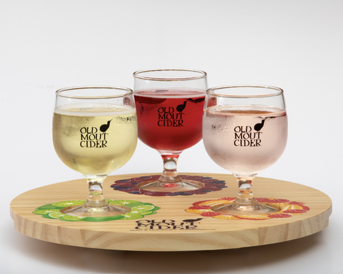 Three glasses of Old Mout Cider in displayed on a round wooden board with matching fruit-themed coasters. Three glasses of Old Mout Cider in displayed on a round wooden board with matching fruit-themed coasters.