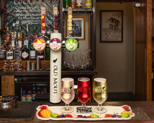 Old Mout Cider draught taps and three filled glasses on a bar counter, with a freshly poured glass being served beside the tap tower. Old Mout Cider draught taps and three filled glasses on a bar counter, with a freshly poured glass being served beside the tap tower.